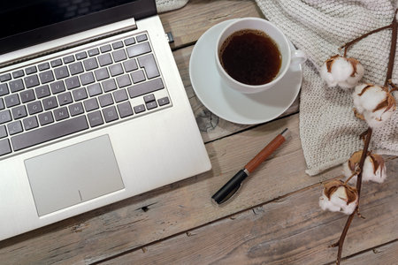 part of a laptop computer keyboard, coffee cup and pen on a rustic wooden table with cotton branch and a white scarf, home office business in autumn, copy space, flat lay, high angle view from above, selected focusの写真素材