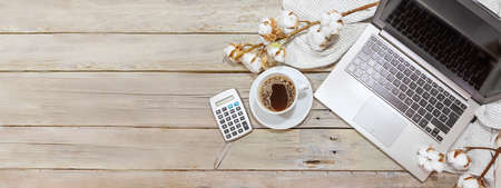 laptop computer, coffee cup and calculator on a rustic wooden table with cotton branches, business and finance accounting in the home office in autumn, panoramic format, copy space, flat lay from above, selected focusの写真素材