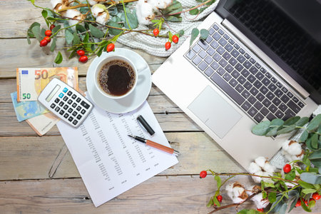 laptop computer, calculator, money and a coffee cup on a rustic wooden table with autumn branches,...