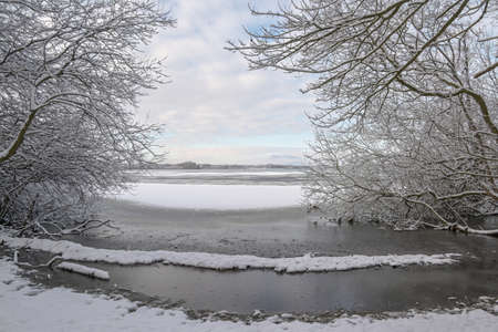View between snow covered bare trees onto the partly frozen lake, winter landscape in north Germany, copy space, selected focusの写真素材