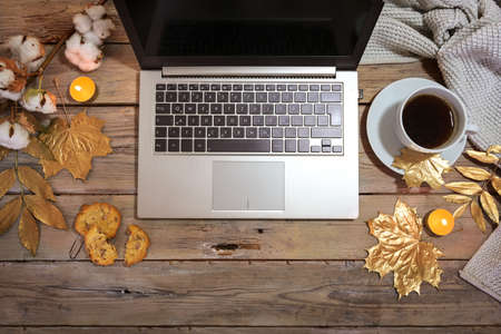 laptop computer and coffee cup on a rustic wooden table decorated with gold painted autumn leaves and candles, cozy home office, flat lay from above, copy space, selected focusの写真素材