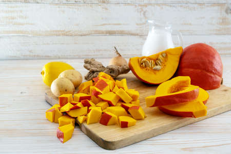 Chopped red kuri squash and ingredients for a vegetarian Thanksgiving or Halloween meal with coconut milk, ginger, potatoes and lemon on a light wooden table, copy space, selected focus, narrow depth of fieldの写真素材