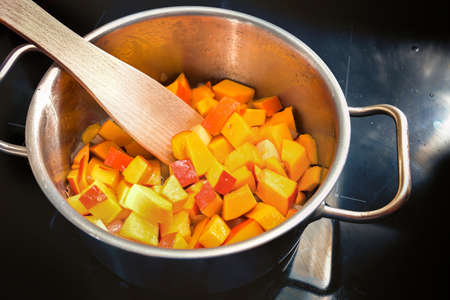 Sliced red kuri squash or Hokkaido pumpkin in a stainless steel pot on a black induction stove, cooking a vegetable recipe for soup or puree in the autumn season, selected focus narrow depth of fieldの写真素材