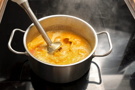 Vegetarian vegetable soup from Hokkaido or red kuri squash is pureed with an immersion blender in a...
