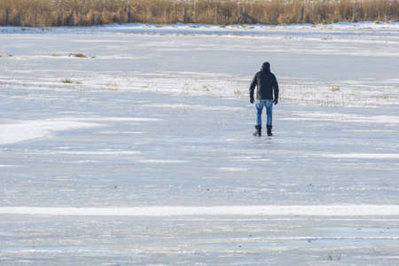 Man from behind standing on the ice of a frozen lake, happy winter activity or dangerous daring in thawing weather, copy space, selected focusの写真素材