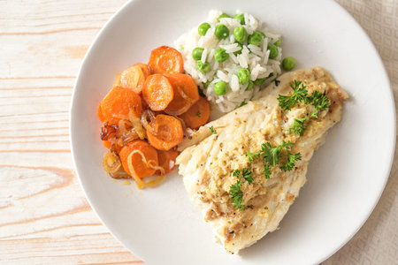 Healthy fish meal from cod fillet with spicy topping and parsley garnish, carrots and green pea rice...