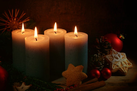 Four lighted candles for advent, Christmas decoration and gingerbread cookies against a dark brown...
