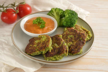 Vegetable patties of broccoli and flaked oats with tomato sauce, vegetarian and vegan meal on a plate and a light wooden table, selected focus, narrow depth of fieldの写真素材