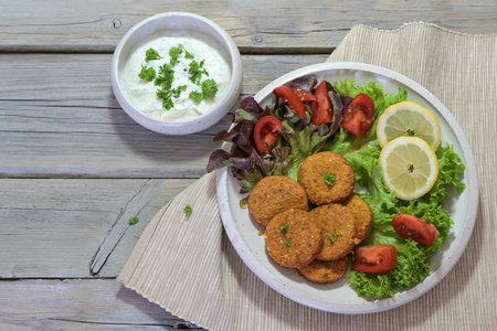 Vegetarian falafel with salad on a plate and yogurt dip in a bowl on a rustic gray wooden table,...