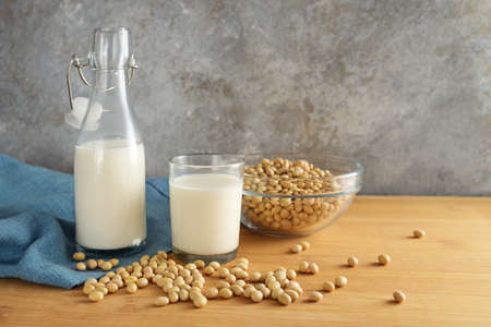 Vegan soy milk in a bottle and a drinking glass and soybeans in a bowl on a wooden table against a rustic wall, alternative to animal dairy products, copy space, selected focus, narrow depth of fieldの写真素材
