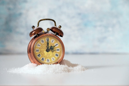 Vintage alarm clock in artificial snow showing clock change to winter time, light blue background...