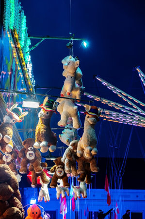 Molln, Germany, November 06, 2021: Large stuffed toys or plushies hanging on a raffle ticket booth at the annual traveling fun fair, colorful lights against a dark blue sky at night, copy space, selected focusのeditorial素材