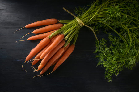 Bunch of organic carrots with green leaves, fresh from the market, on dark rustic wood, copy space,...