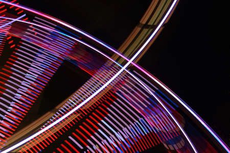 Abstract long exposure of a spinning Ferris wheel and a fast ride on a fun fair at night, colorful light traces in motion blur against a dark sky, copy spaceの写真素材