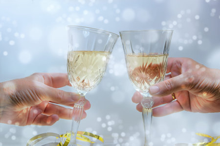 Two hands toast with champagne glasses on a New Year or Christmas party, light snowy background,...