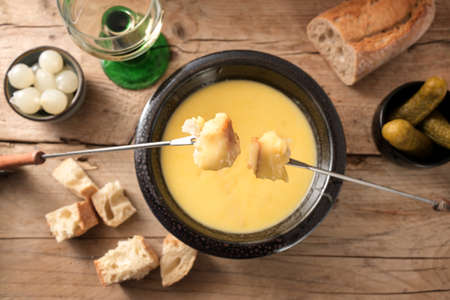 Fondue from melted cheese with bread on long forks, pickles and wine on a rustic wooden table, traditional new year dish from Switzerland, copy space, high angle view from above, selected focusの写真素材