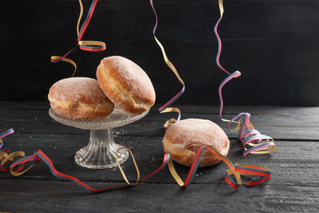 Berliner donuts or Krapfen with colorful party streamers on a dark rustic wooden table, traditional...
