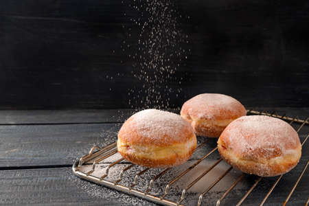 Krapfen or Berliner donuts on a baking grid are sprinkled with sugar, fried pastry for New Year or carnival, dark rustic wooden background, copy space, selected focus, narrow depth of fieldの写真素材