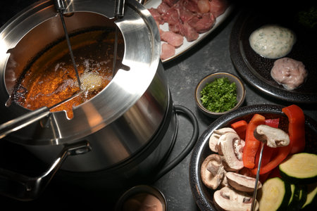 Fondue pot with hot oil, long forks, vegetables and raw meat, festive party dinner for friends and...
