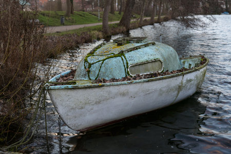 Abandoned small cabin boat made of glass fiber reinforced plastic overgrown with moss and lichen on...