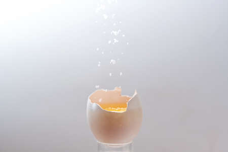 Cracked egg with yellow yolk is sprinkled with falling salt crystals, light gray background with copy space, motion blur, selected focus, narrow depth of fieldの写真素材
