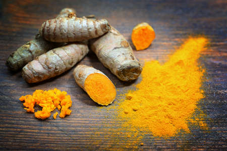 Turmeric roots, whole, fresh grated and dry powder on a dark rustic wooden table, Asian spice for health, anti-inflammatory and antioxidant, copy space, selected focus, narrow depth of fieldの写真素材