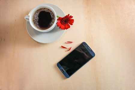 Cell phone, coffee cup and a red flower with torn out petals as yes or no oracle, love and dating call concept, light wooden background, copy space, high angle view from above, selected focusの写真素材