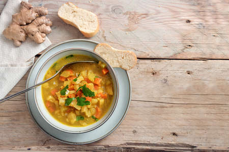 Vegetable soup from carrot and celery with ginger and parsley in a bowl on a rustic wooden table, vegan and vegetarian dish for a healthy diet, copy space, top view from above, selected focusの写真素材