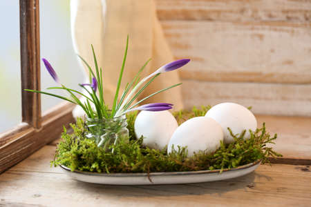 Natural Easter decoration with crocuses and eggs on moss arranged on a plate on a rustic wooden table by the window, copy space, selected focus, narrow depth of fieldの写真素材