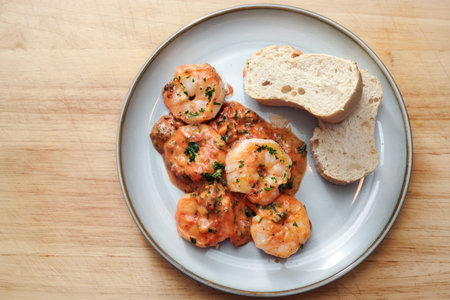 Shrimps in tomato sauce with bread on a plate and a wooden table, copy space, high angle view from above, selected focusの写真素材