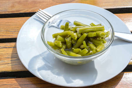 Small side salad of pickled green beans with onions and herbs in a glass bowl on a white plate with a fork, selected focus, narrow depth of fieldの写真素材