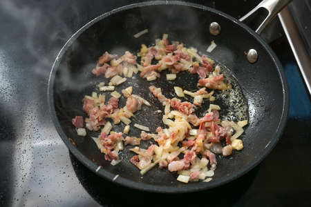 Bacon and onions fry in a hot steaming pan on the stove, cooking at home, copy space, selected focus, narrow depth of fieldの写真素材