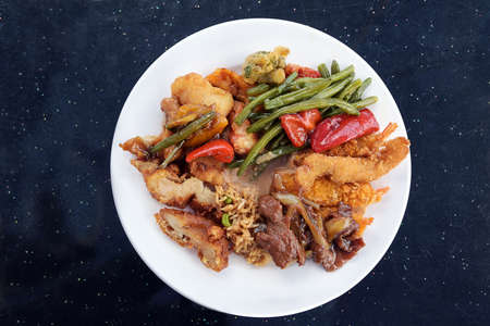 Chinese food, various meat and vegetables with fried rice and sauce on a white plate and a dark table with sparkling dots, copy space, high angle view from aboveの写真素材