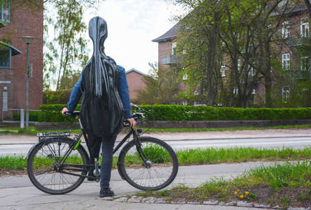 Young musician with a black cello case on his back stands with his bicycle in a suburban street in a residential area on the way to music lessons or to an apartment tour, selected focusの写真素材