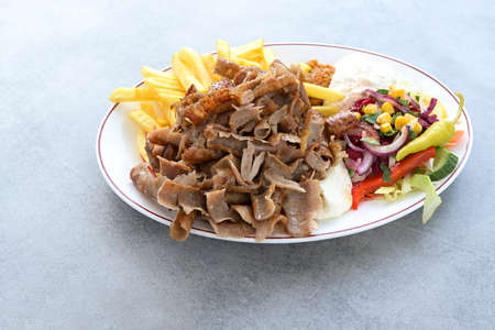 Thin slices of doner kebab meat with french fries, salad and yogurt dip sauce on a plate and a gray table, copy space, selected focus, narrow depth of fieldの写真素材