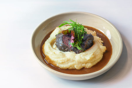 Traditional ox cheeks on potato puree with brown red wine sauce and garnish from wild herb leaves in...