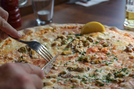Hands with cutlery cutting a pizza with seafood in an Italian restaurant, food and drink concept,...