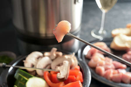 Piece of raw meat skewered on a long fondue fork and some vegetables to be fried in a pot with hot oil, festive dinner for joint evenings with friends and family, selected focus, very narrow depth of fieldの写真素材
