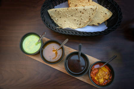 Indian dip, relish, chutney and sauce served in small black bowls with crispy papadam bread on a dark wooden table, copy space, high angle view from above, selected focusの写真素材