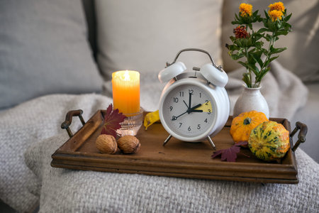 Vintage alarm clock showing one hour fall back after daylight saving time, wooden tray with candle...