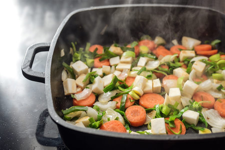 Steaming chopped vegetables in a black cooking pan, ingredients for soups or sauces with carrots,...