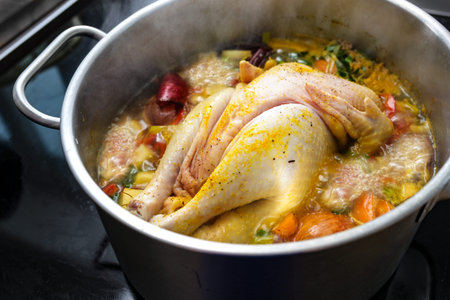 Chicken soup with vegetables and spices is boiling in a pot, cooking a healthy broth, home remedy...
