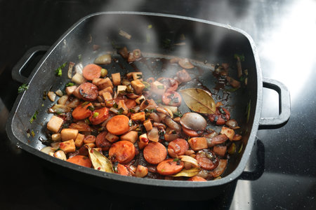 Roasted vegetables for a tasty sauce base in a black cooking pan with carrots, onions, leeks, celery and bay leaves, copy space, selected focus, narrow depth of fieldの写真素材