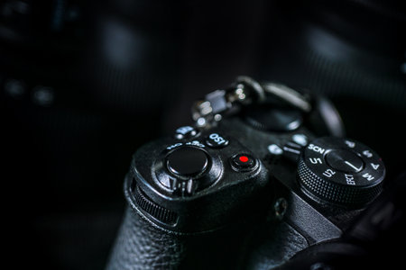 Detail of a digital photo camera, adjustment dials and knobs on the top of the black body, technical equipment for business or hobby, dark background, copy space, selected focus, narrow depth of fieldの写真素材