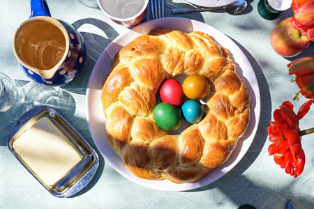 Traditional Easter plait in wreath shape baked from a slightly sweet yeast dough with colorful eggs in the center on a set table outside in the sun, high angle view from aboveの写真素材
