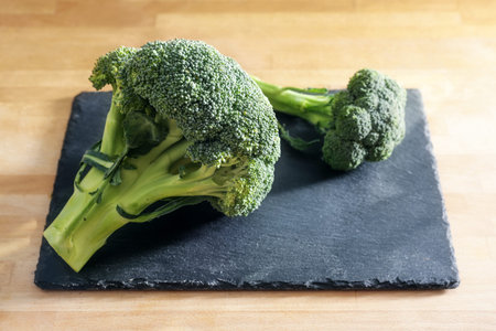 Raw broccoli on a slate plate and a wooden kitchen table, preparation for cooking vegetables,...