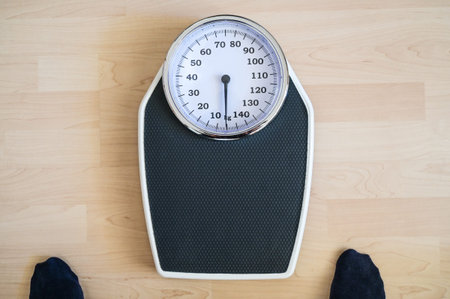 Analogue old-fashioned personal scale on a wooden floor, two feet in dark stockings hesitantly...