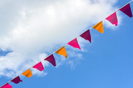 Pennants in pink, orange and purple hanging diagonally on a line against a blue sky and a white...