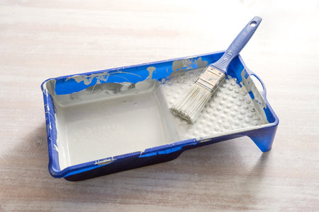 Blue paint tray with light gray lacquer and a brush on a wooden table, craft concept for renovation, painting and do it yourself, copy space, selected focusの写真素材