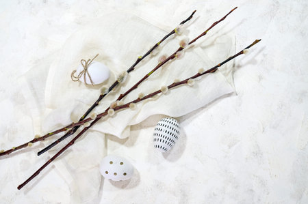White Easter eggs with small black decor and some willow branches with catkins on a light cloth and...